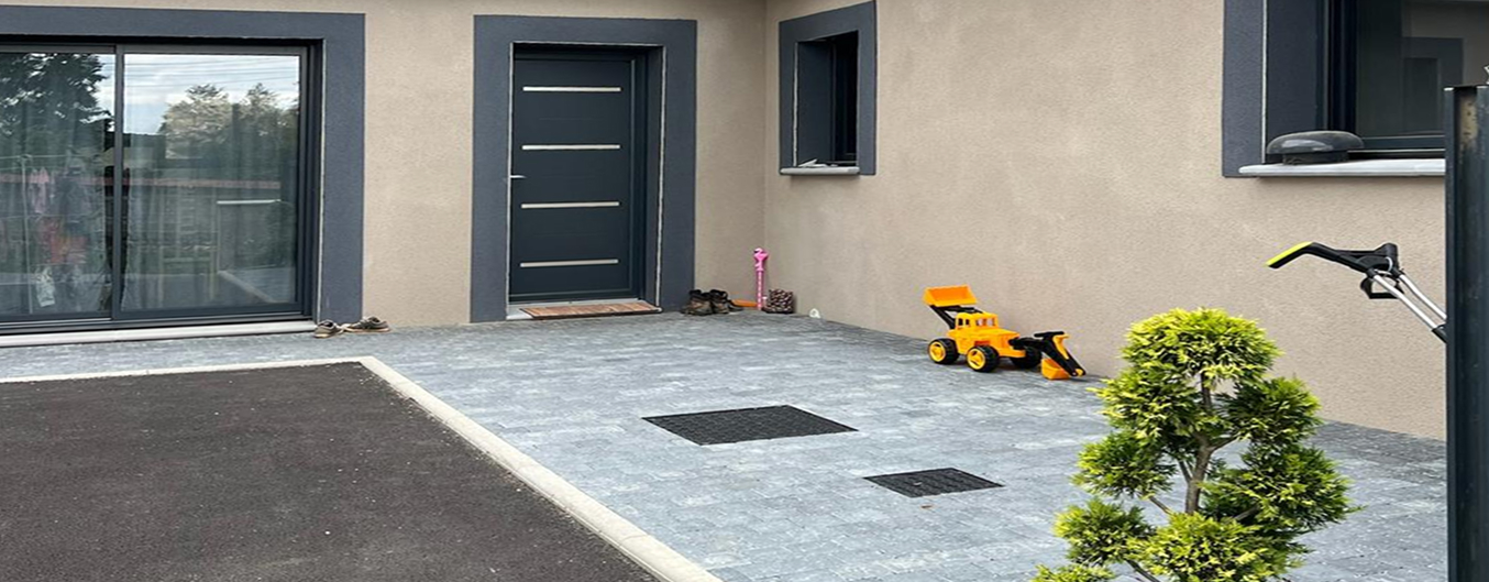 Pose de bordure et pavés gris autour d’une cour en enrobé, entrée de maison moderne avec massifs et finitions nettes