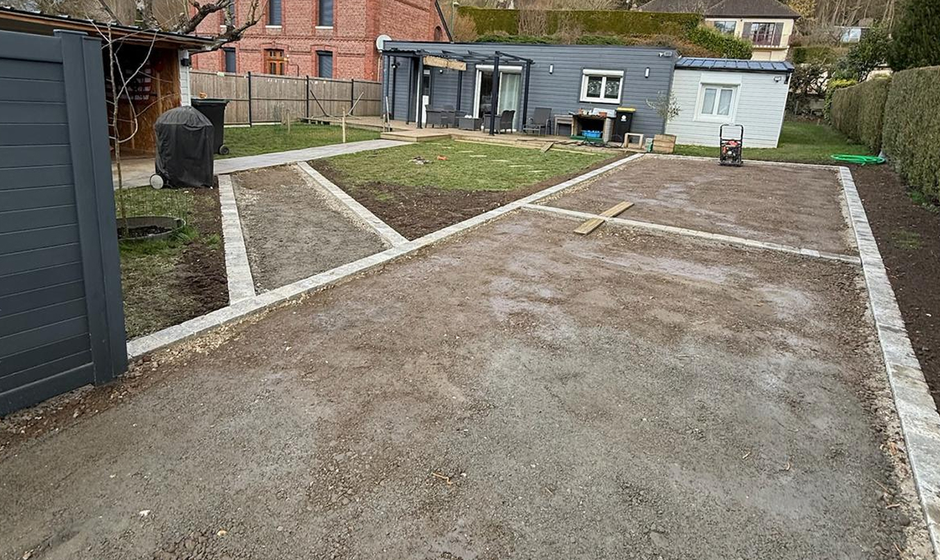 Pose de bordure en pierre le long d’une cour en gravier compacté, vue d’ensemble avec caniveau et portail au fond.