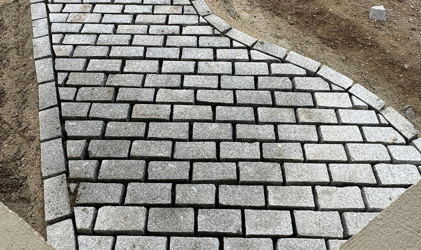 Pose de pavé en granit sur une allée courbe, pavés gris alignés avec bordures, chantier de terrassement autour.