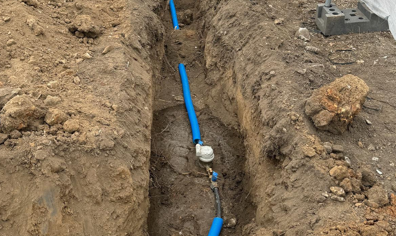 Tranchée technique en cours de pose d’un réseau d’eau, tuyau bleu dans l’excavation, terre excavée sur les côtés.