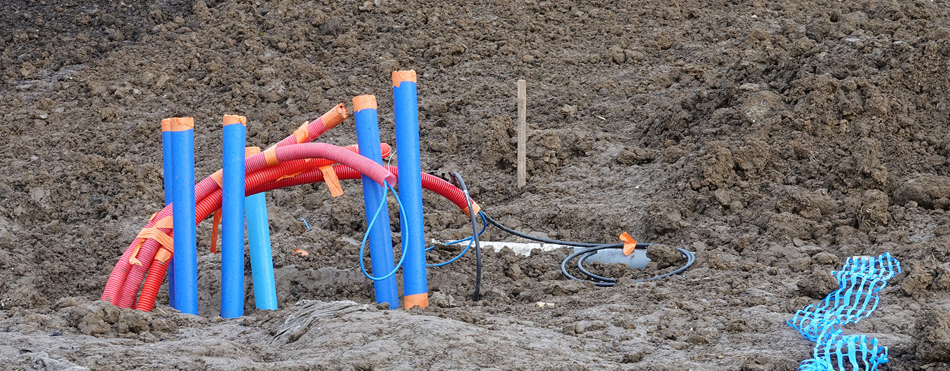 Viabilisation chantier : passage de fourreaux bleus et gaines rouges pour réseaux, zone de terrassement en arrière-plan.