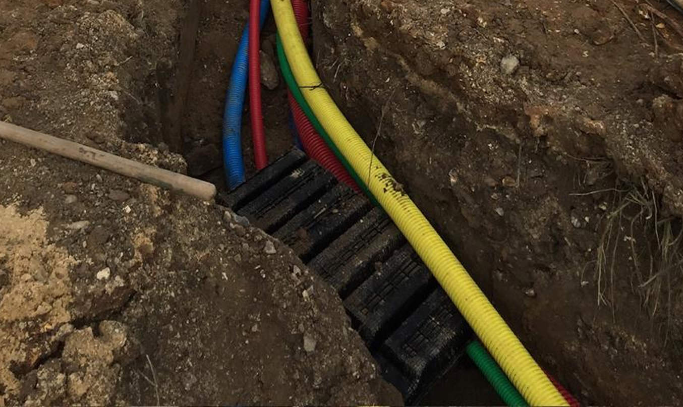 Viabilisation de maison : pose de gaines rouges, jaunes, vertes et bleues dans une tranchée, chantier de raccordement.